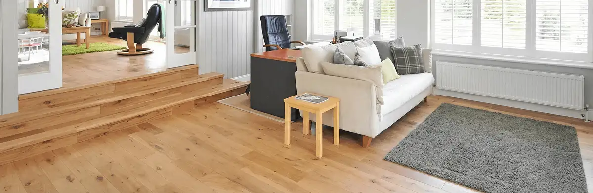 A modern living room with professionally installed laminate flooring, a beige sofa, a small side table, a gray rug, and large windows with white shutters in Clearwater, FL